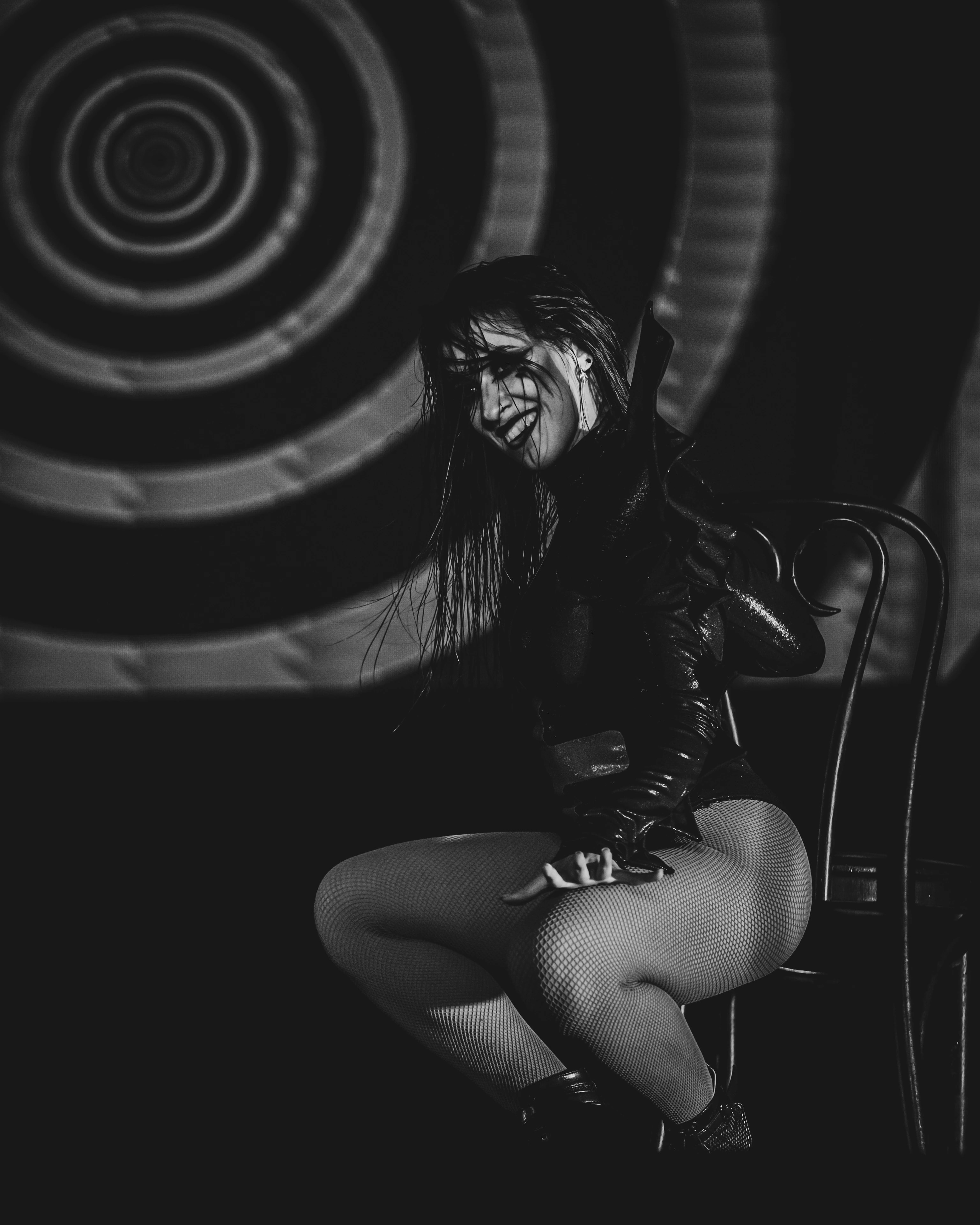 Black-and-white stage photograph of Lourdes seated in dramatic makeup against circular stage projections