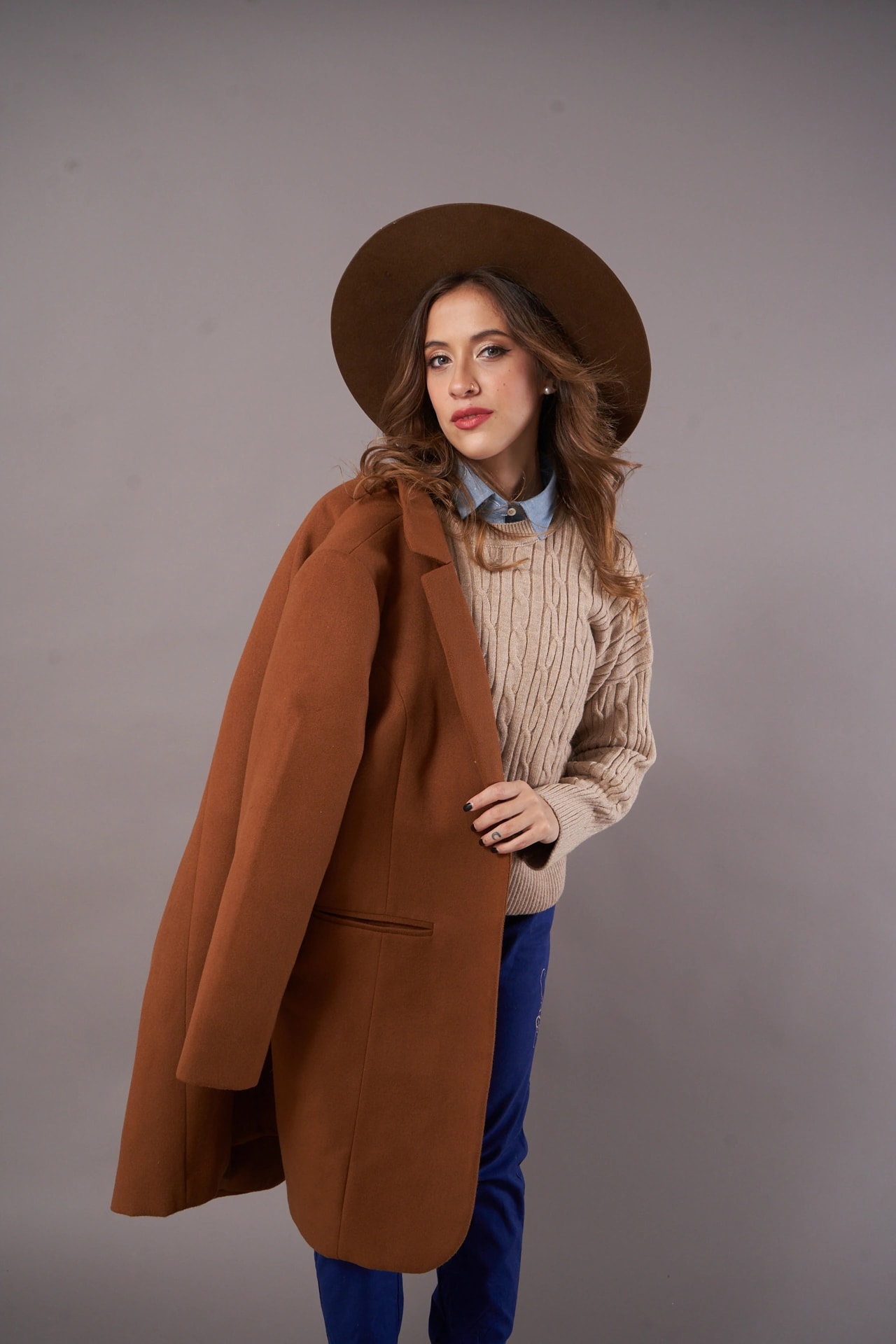 Lourdes modeling a brown coat, knit sweater and wide-brimmed hat in the studio