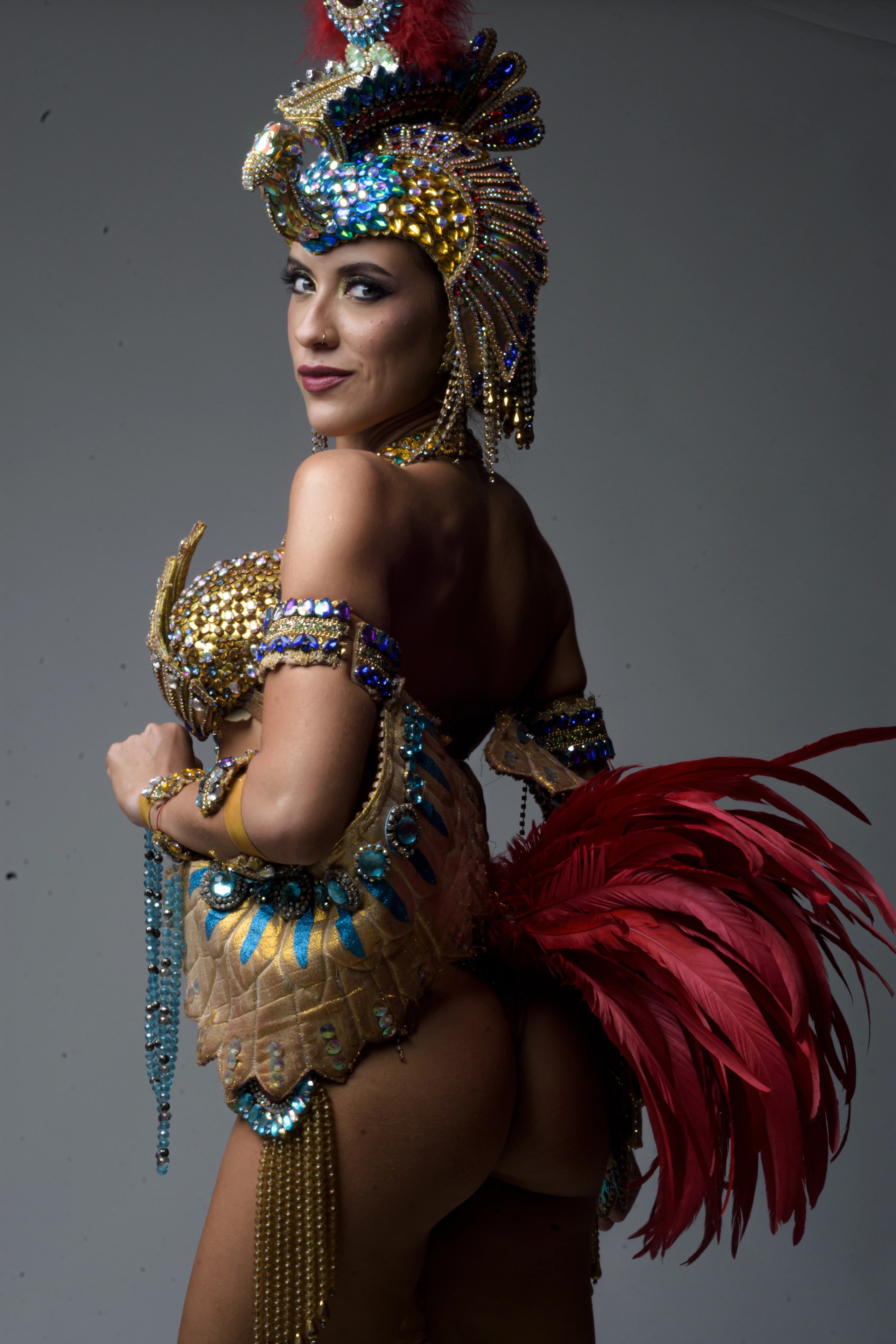 Studio portrait of Lourdes in a jeweled gold and turquoise carnival costume with red feathers