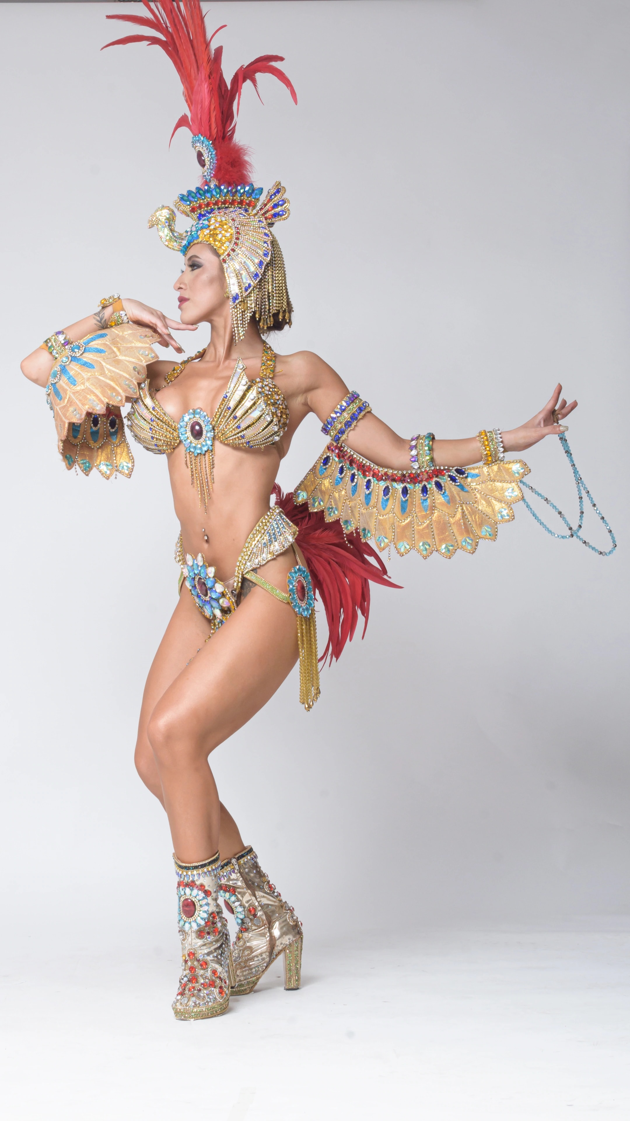 Lourdes in a gold carnival costume, feathered headdress and an extended dance pose in the studio